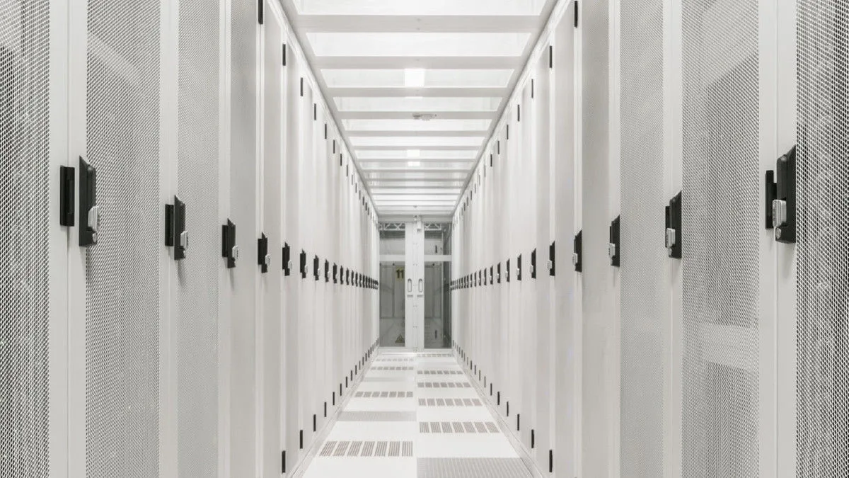 I’m inspecting the attached hero image so the alt text accurately describes its visible content.  A bright white server room corridor lined with rows of data center racks.